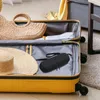 An open yellow suitcase filled with travel items, including a straw bag, hats, and clothing, with a black insulin cooling bag placed inside. Produktbild-Vorschau