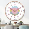 A colorful wall clock with numbers and flower-shaped petals is displayed on a white wall. Produktbild-Vorschau