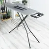 A gray ironing board with a black frame and an attached sleeve board is set up on a light gray wooden floor, with a white shelf unit and some plants in the background. Voir les images du produit
