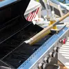 A grill brush is being used to clean a gas grill on an outdoor patio. Produktbild-Vorschau