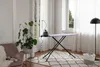 A well-lit room with a plant, armchair, ironing board, and laundry basket. Voir les images du produit