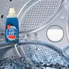 A bottle of anti-limescale cleaner is placed inside a washing machine drum with water splashing. Náhled obrázku produktu