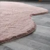 A close-up view of a pink, fluffy rug with a wavy edge, lying on a grey wooden floor. Produktbild-Vorschau