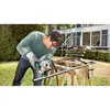 A man is using an angle grinder to cut a metal pipe outdoors in front of a house. Produktbild-Vorschau