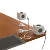 Two white PowerCube devices are shown on a wooden desk, one is elevated and attached to the desk with a mount, the other is on the edge of the desk. A tablet is also visible on the desk. Produktbild-Vorschau