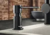 A black soap dispenser is shown on a kitchen counter next to a sink, with a brick wall in the background. Produktbild-Vorschau
