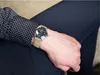 A person wearing a watch on their wrist, with a polka dot shirt and dark pants. Voir les images du produit