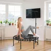 A woman is exercising on a mini trampoline in a bright, modern living room. Produktbild-Vorschau