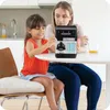 A mother and daughter are sitting at a table in a kitchen, interacting with a black and silver electronic piggy bank. Náhled obrázku produktu