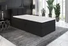 A black boxspring bed with a white mattress and topper is shown in a bedroom setting with plants and decorative elements. Produktbild-Vorschau