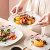 A person is holding a plate of seafood and vegetables, with other plates of food on a table. Voir les images du produit
