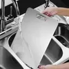 A person is rinsing a stainless steel cutting board under a faucet in a kitchen sink. Náhľad obrázku produktu