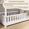 A white wooden bed with a safety barrier, with text overlays describing its features. Produktbild-Vorschau