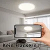 A hand holding a smartphone showing a ceiling light, with a living room in the background. Voir les images du produit