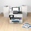 A Canon MAXIFY GX 7050 Multifunction Printer is shown on a wooden desk, surrounded by stacks of paper and printed brochures. Produktbild-Vorschau