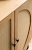 A close-up view of a wooden sideboard with rattan woven door panels and black handles. Produktbild-Vorschau