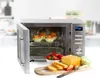 A microwave oven with its door open, showing muffins inside, and a selection of baked goods and strawberries in front of it. Náhled obrázku produktu