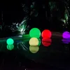 Several illuminated spherical lights are floating on a dark reflective surface, possibly a pool, at night. Lush green foliage is visible in the background, illuminated by spotlights. Voir les images du produit