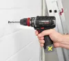 A person is using a cordless drill to drill a hole in a white brick wall. A ladder is visible in the background. Produktbild-Vorschau