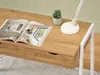 A close-up view of a wooden desk with a magazine, a small plant, and a desk lamp. Voir les images du produit