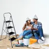 A couple is sitting on the floor next to a ladder, surrounded by painting supplies, suggesting they are about to start a home renovation project. Náhled obrázku produktu