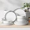 A collection of white ceramic dinnerware with black trim, arranged on a light-colored surface. Náhled obrázku produktu