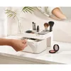 A hand is shown opening a drawer of a makeup organizer on a white surface, with makeup brushes and other cosmetics inside. Náhled obrázku produktu