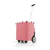 A pink shopping trolley with a white handle and black wheels, isolated on a white background. Produktbild-Vorschau