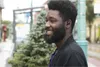A man wearing earbuds smiles while standing outside. Anteprima dell’immagine prodotto