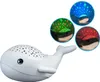 A white whale-shaped night light projector is shown on a white background. Three circular insets display the whale projecting different colored starry sky patterns. Produktbild-Vorschau