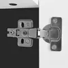 A close-up view of a cabinet hinge attached to a white surface and a black surface. Náhľad obrázku produktu