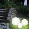 Three illuminated spherical garden lights are placed on a grassy lawn next to a stone pathway and steps. Produktbild-Vorschau