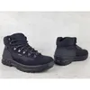 Two black hiking boots are displayed on a light gray concrete surface. Podgląd zdjęcia produktu