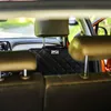 View from the back seat of a car, looking forward at the back of the front seats. A black quilted seat protector is attached to the back of the driver's seat. Produktbild-Vorschau