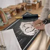A person is using a rolling pin on a black silicone baking mat with flour on it, in a kitchen setting. Voir les images du produit