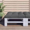 A close-up view of a grey pallet cushion on a white wooden pallet base, placed on a wooden deck, with a slatted wooden fence in the background. Produktbild-Vorschau