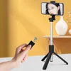 A hand holding a remote control for a selfie stick with a phone mounted on it, showing a person applying makeup. Voir les images du produit