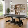 A massage table in a clean, well-lit room with shelves of towels and bottles. Produktbild-Vorschau