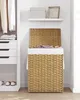 A woven laundry basket with a white liner and a few items of clothing inside, placed next to a white closet with hanging clothes and drawers. Produktbild-Vorschau