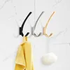 Three wall hooks in different colors (black, silver, gold) mounted on a tiled wall. A yellow towel is hanging on the black hook, and a loofah is hanging on the gold hook. Produktbild-Vorschau