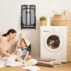 A mother and daughter are sitting on the floor in a laundry room, surrounded by clothes. An ironing board is mounted on the wall behind them, and a washing machine is to the right. Produktbild-Vorschau