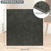 A dark gray square tile with dimensions and thickness indicated, placed on a light-colored floor with a blurred background of a room. Náhled obrázku produktu