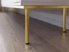 A close-up view of the gold legs and bottom edge of a white cabinet or TV stand, resting on a wooden floor. Náhled obrázku produktu