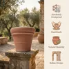 A terracotta pot is displayed outdoors on a stone pedestal, with olive trees and stone architecture in the background. To the right, there are icons and text describing product features. Produktbild-Vorschau