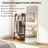 A full-length mirror is shown in a bedroom setting, next to a wooden garment rack with clothes hanging on it. The mirror reflects a bed and a painting on the wall. Náhled obrázku produktu