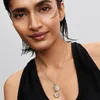 A close-up shot of a woman wearing a necklace with two charms. Anteprima dell’immagine prodotto