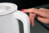 A close-up shot of a person's hand pressing a button on the handle of a white electric kettle. Produktbild-Vorschau