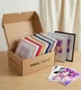 A cardboard box filled with framed pictures and loose photos, with two framed pictures standing behind it. Produktbild-Vorschau