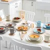 A dining table set for a meal with plates, bowls, cutlery, glasses, and food. Náhled obrázku produktu