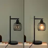 A split image showing a black metal table lamp with a vintage-style bulb. The left side shows the lamp unlit, and the right side shows it lit. Podgląd zdjęcia produktu